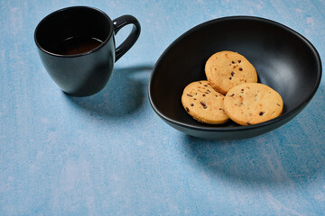 coffee cup and a black bowl with cookies on a blue background