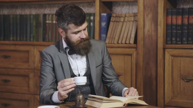 Mature man in library and enjoys reading. Bearded man in suit looks satisfied. Relax pleasure and leisure, hobby concept. Literature and success. Drink coffee or tea. Professor.