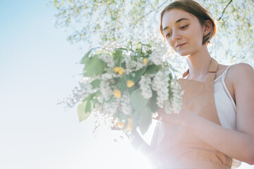 Portrait of beautiful woman making wreath of flowers dandelions on flowering field. Summer lifestyle, nature lover and freedom concept. Florist workshop. Romantic background of florist at work.