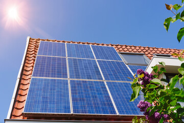 Solar panel on a red roof reflecting the sun and the cloudless blue sky