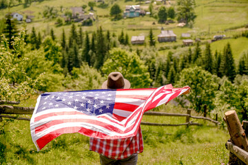 A young woman stands on a mountain and holds the US flag in her hands. American Independence Day celebration.