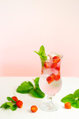Strawberry drink.Refreshing summer cocktail.Summer drink.mineral water glass with ice and strawberries and strawberries with leaves on a pink background.Drink from summer berries