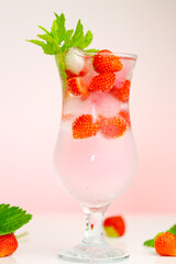 Strawberry drink.Refreshing summer cocktail.Summer drink.mineral water glass with ice and strawberries with leaves on a pink background.Drink from summer berries