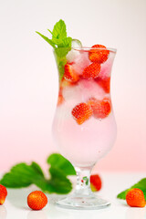 Strawberry drink.Refreshing summer cocktail.Summer drink.mineral water glass with ice and ripe strawberries with leaves on a light pink background.Drink from berries