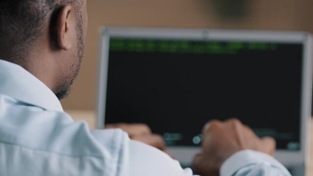 Back rear view of unrecognizable african young man working at computer IT programmer engineer specialist data scientist developing software app browsing code on screen coding internet security system