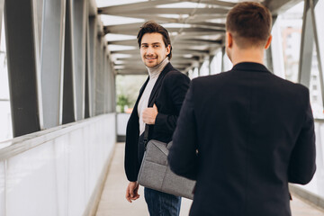 Fototapeta premium Two modern businesspeople greet each other smiling and saying something against the background of urban offices and buildings