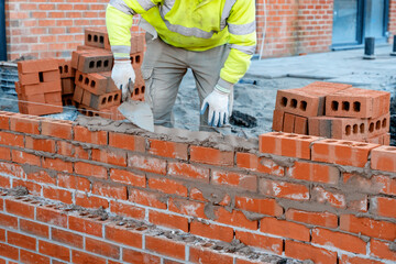 Bricklayer in safety vest and a helmet laying a brick wall using a trowel