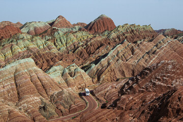 De bus die de woestijnweg oversteekt langs de Chinese regenboogbergen van Zhangye Danxia National Geological park