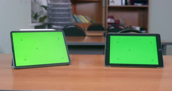 Two black tablets with a chrome green display stand on a desk in a classroom or auditorium. Distance learning during the pandemic and isolation. Business training, webinar, remote employee training.