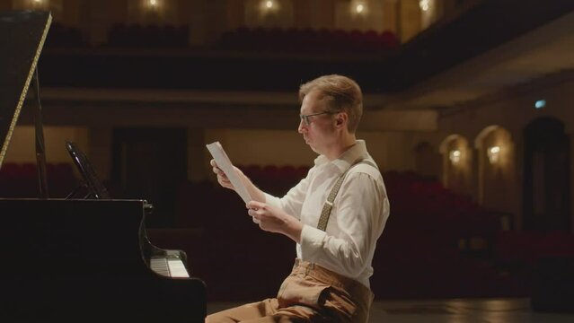 Arc slow mo shot of pianist throwing away sheet music and playing grand piano on stage in concert hall