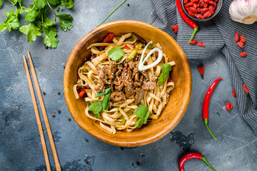 fried Udon with beef and vegetables on wooden bowl on grey table top view