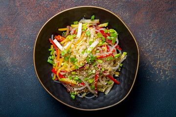 Rice noodles with vegetables, vegetarian noodles on a black bowl on blue concrete table