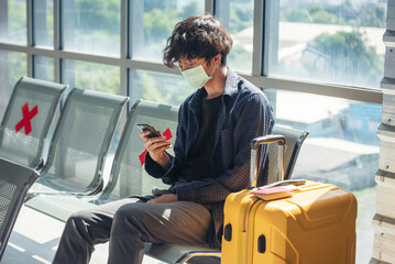 Asian young man traveller new normal holding smartphone in Airplane lounge wear face mask sitting...