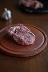 A piece of raw beef is lying on a wooden Board in the kitchen