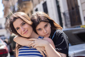 life style portrait of brunette sisters hugging on a city street on a Sunny windy day