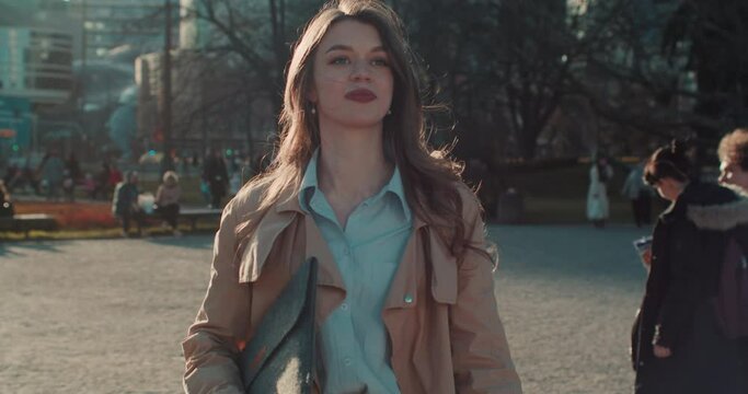 Back lit shot of beautiful young confident Caucasian businesswoman with laptop walk to camera in sunny park slow motion.