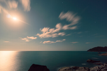 Full moon rising over sea and rocks on the beach