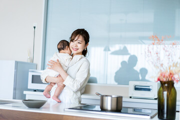 赤ちゃんを抱っこしながら家事をする若い女性