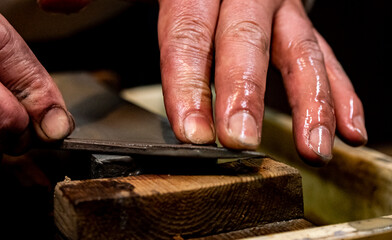 Master swordsmith is sharpening knife on grindstone with water