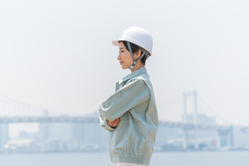 真剣な顔で腕組をする建築着を着た日本人女性・青空バック