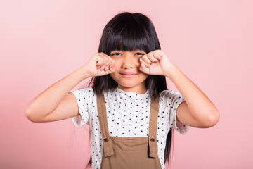 Unhappy children. Asian little kid 10 years old bad mood her cry wipe tears with fingers at studio shot isolated on pink background, child girl stress feeling sad unhappy crying