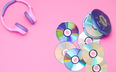 Personal compact portable CD player disks purple headphones on a pink background.