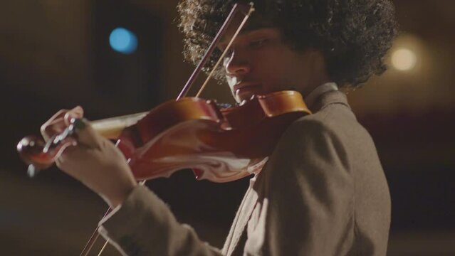 Low angle selective focus shot of young African American violinist playing fiddle during classical music concert
