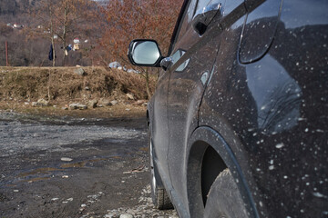 A black SUV in the mud stands at the foot of the mountain. The car is splashed with mud against the backdrop of the autumn mountains. There is a mountain obstacle ahead. Selective focus.