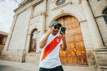 Hincha peruano de futbol celebrando un gol mirando su telefono en un parque de peru. Concepto de Personas y deportes. - obrazy, fototapety, plakaty
