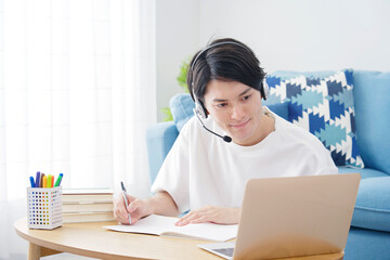 リビングでヘッドセットをつけてパソコンを見て勉強する男性