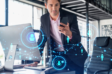 Businessman in suit using smart phone to check new candidates for international business consulting. HR, social media icons over modern panoramic office background.