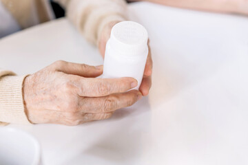 Close up hands of a senior woman holding a medical bottle and asking for information from the nurse before administering medication. Caregiver visit at home. Home health care and nursing home concept.