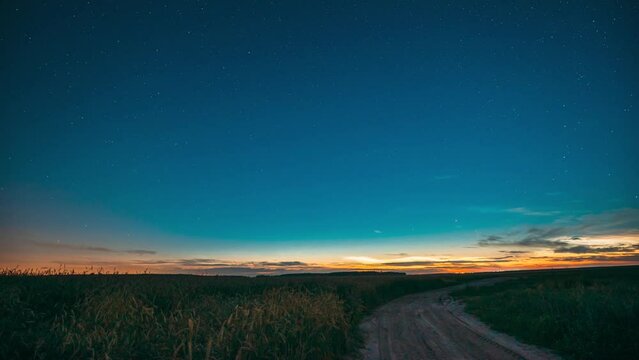Time Lapse Night Starry Sky With Glowing Stars Above Countryside Landscape With Country Road And Wheat Fields. Noctilucent Clouds Above Rural Wheat Field In Summer. Summertime. TimeLapse Time-Lapse.