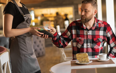 caucasian man paying through payment terminal in hands of waitress, paying with credit card in cafe, customer making contactless payment with debit card