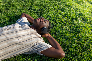 Black man relaxing outdoors. Happy black male lying on grass listening to music with headphones....