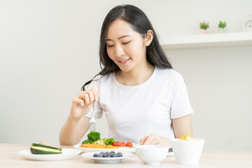 Obraz na płótnie Canvas Dieting, diet asian young woman, girl eating, holding fork at broccoli, diet plan nutrition with fresh vegetables salad, enjoy meal on table at home. Nutritionist of healthy, nutrition of weight loss.