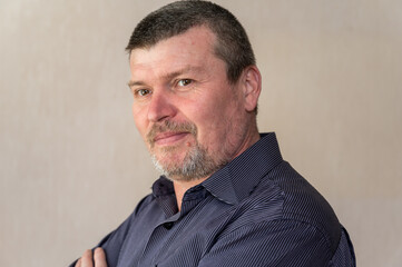 Portrait of a grown man with his arms crossed over his chest. Man in blue striped shirt. Side view. Inside the room. Selective focus.