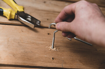 The process of screwing a half-ring screw into a board. The man's hand screws the C-shaped screws into the drilled holes. Close-up. Selective focus.