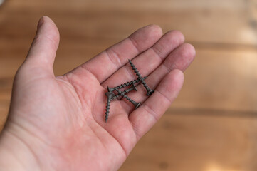The black self-tapping screws lie in the palm of my hand. Five black screws lie in a man's hand. First-person view. Selective Focus.