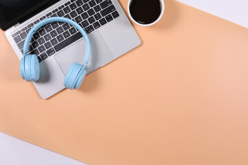 Light blue headphone placed on laptop with black coffee cup isolated on orange and white background. Flat lay photography with copy space.