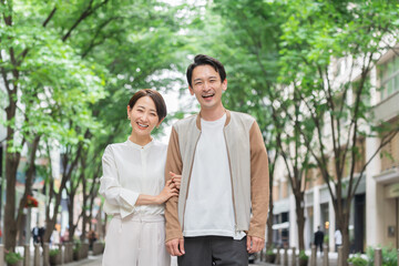新緑バックで笑顔のカメラを見る30代日本人のカップル・夫婦