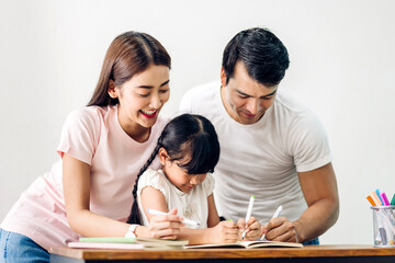 Portrait happy love asian family father and mother with little asian girl learn and study on table.Mom and dad with asian young girl writing with book make homework in homeschool at home.Education
