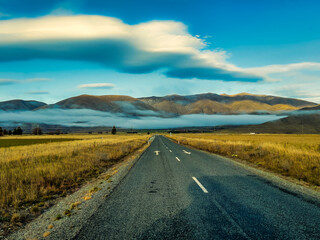 Fototapeta premium The asphalt road heading to the fluffy cloud both above and below the hills