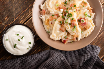 Potato dumplings with sour cream on the wooden table. Traditional ukrainian food. Varenyky, vareniki, pierogi, pyrohy - dumplings with filling.