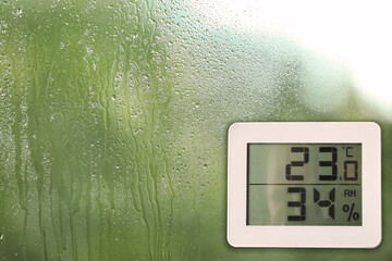 Digital hygrometer with thermometer on glass with water drops. Space for text