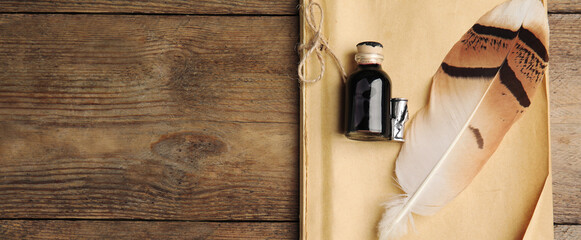 Quill, bottle of ink and notebook on wooden table, top view with space for text. Banner design