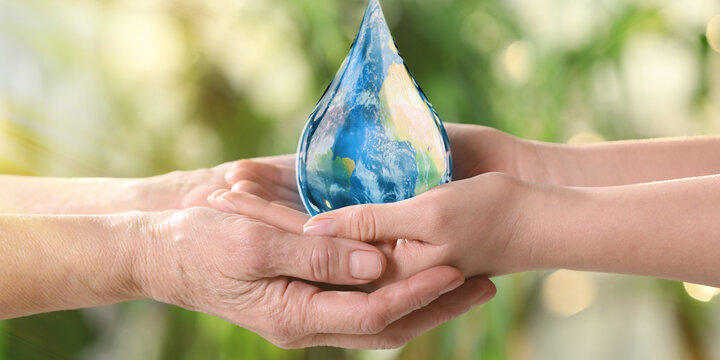World Water Day. Young and elderly women holding icon of drop with Earth image inside on blurred green background, closeup