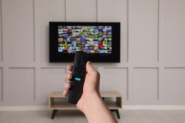Woman with remote control changing channels while watching TV at home, closeup
