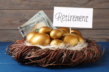 Golden eggs, dollar banknotes and card with word Retirement in nest on blue wooden table. Pension...