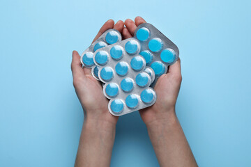 Fototapeta na wymiar Woman holding blisters with cough drops on light blue background, top view